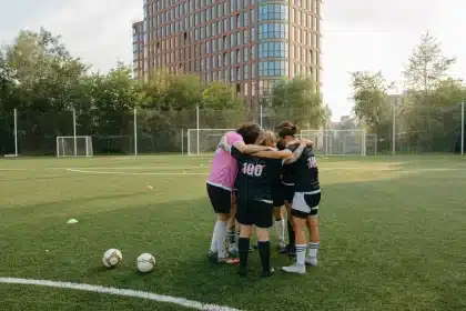 Treino de futebol com jogadores no relvado e equipa técnica ao fundo