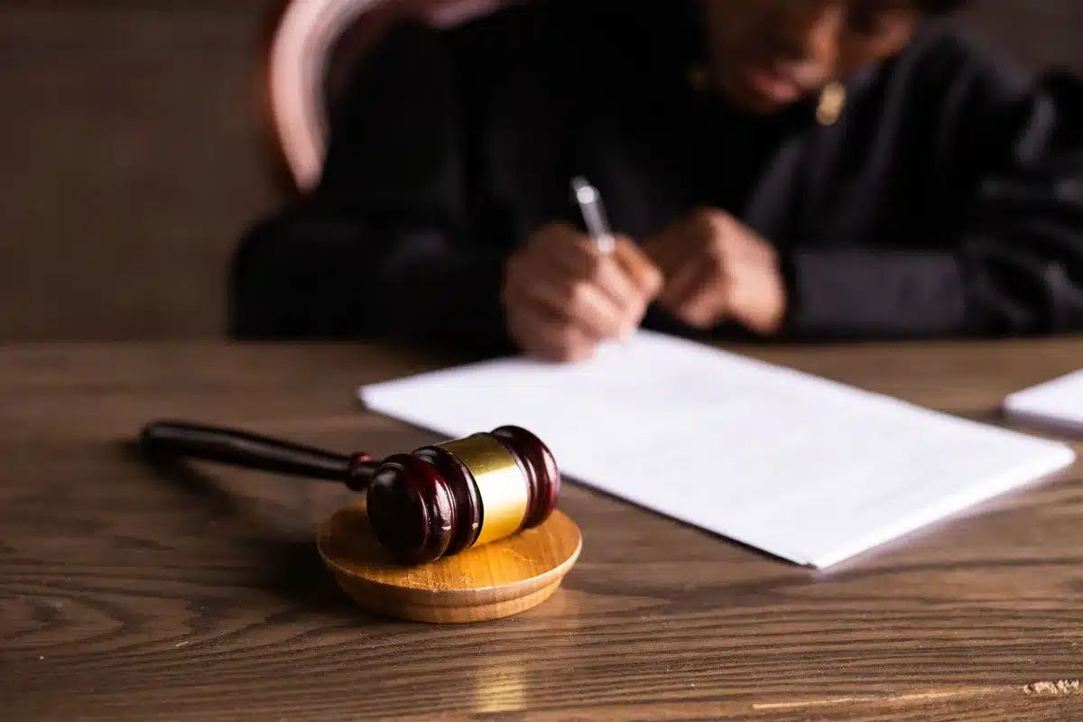 Sala de tribunal com juiz e documentos processuais sobre a secretária