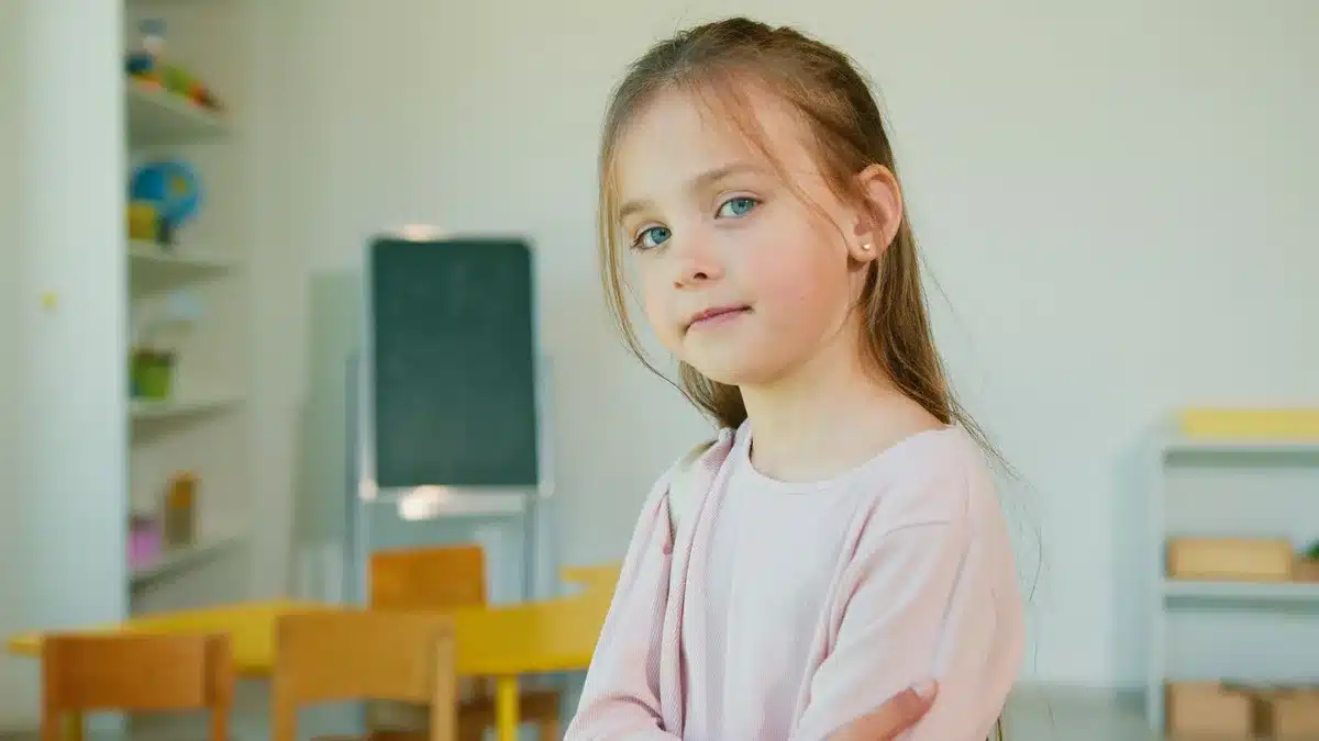 Criança sentada ao computador, relutante em ir para a escola, com edifício escolar ao fundo