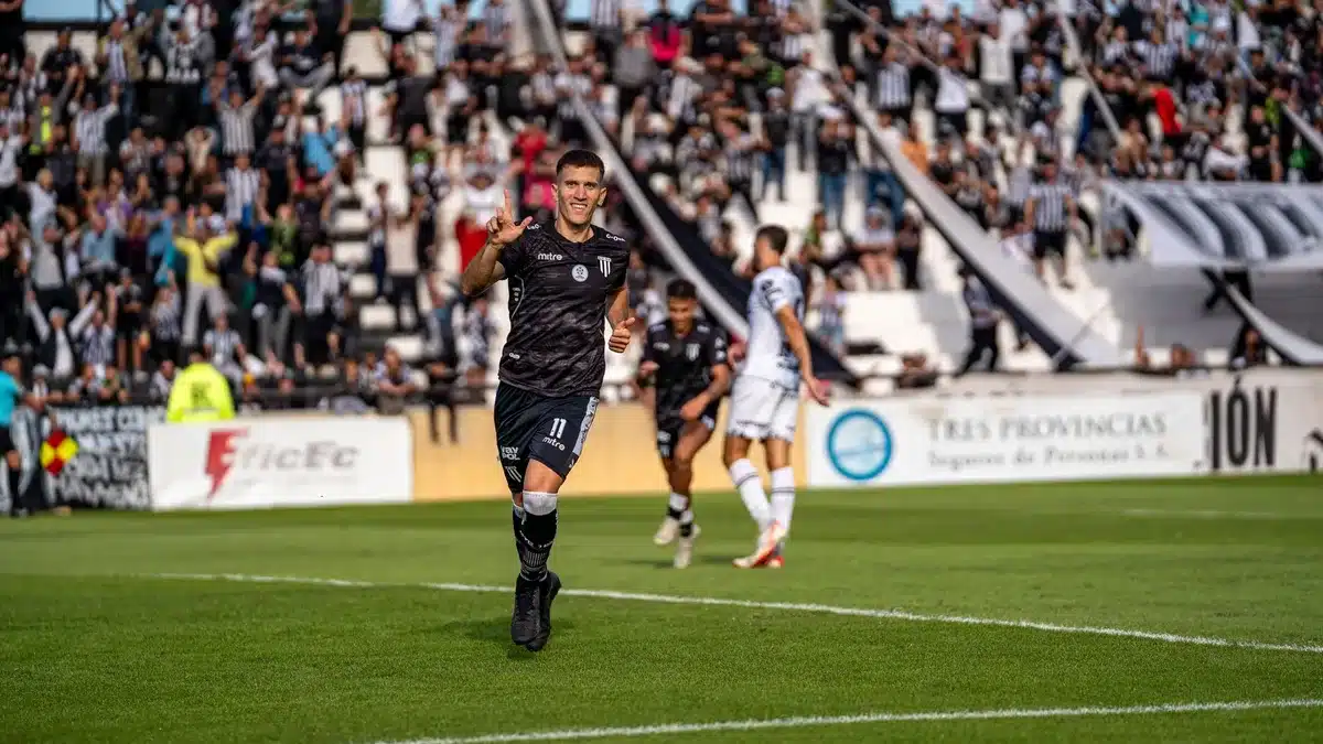 Jogador de futebol a celebrar um golo com os braços levantados, luzes do estádio ao fundo.
