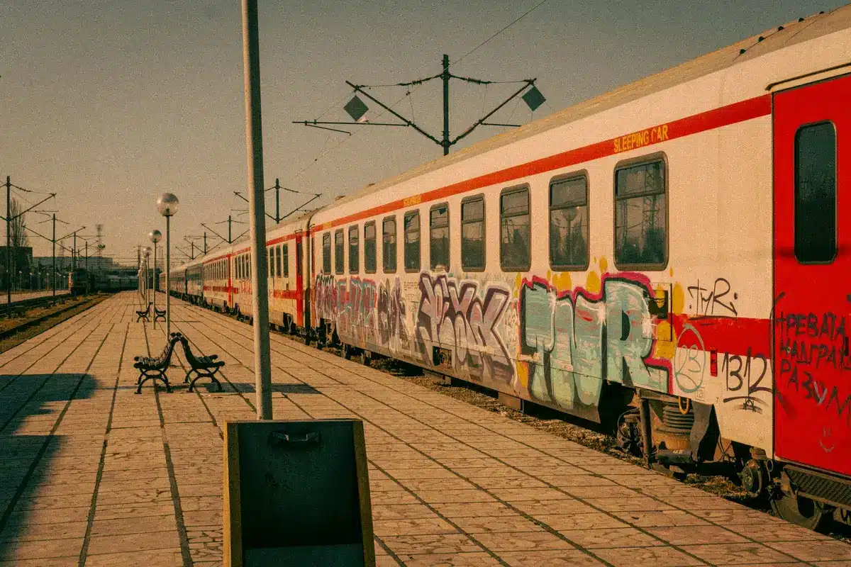 Estação ferroviária em cenário urbano europeu com comboios e viajantes ao fundo