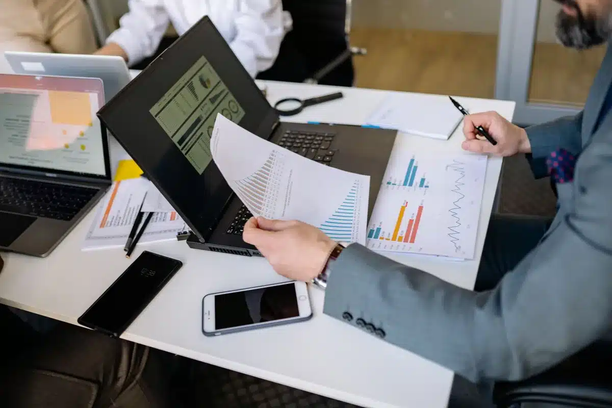 Jornalista em secretária de redação com gráficos financeiros e dados económicos no computador