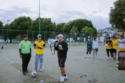 Treinador de futebol a orientar treino com jogadores ao fundo num estádio iluminado