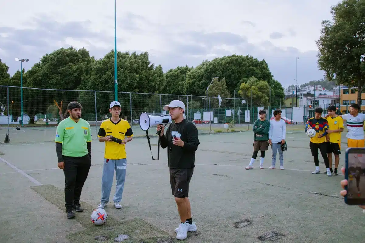 Treinador de futebol a orientar treino com jogadores ao fundo num estádio iluminado