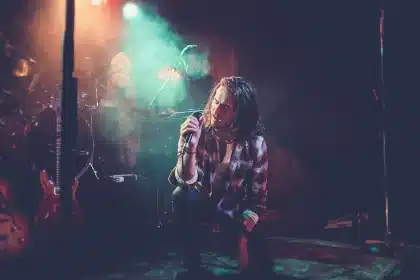 Silhuetas anónimas de dois artistas num palco com luz quente e um roteiro dobrado.