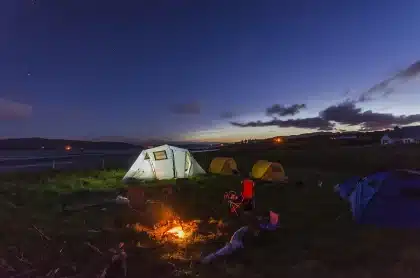 Pessoas reunidas à volta de uma fogueira durante um acampamento noturno