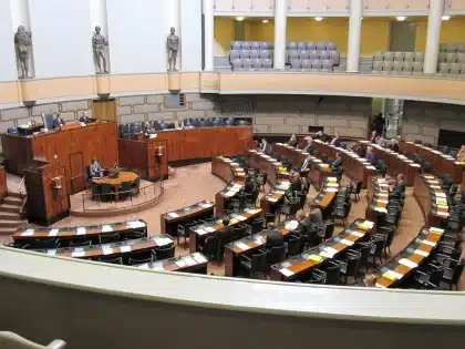 Sala de imprensa governamental com pódio vazio e silhuetas ao fundo
