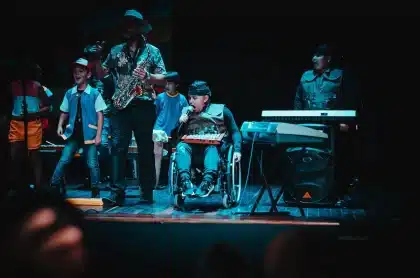 Palco de festival ao ar livre com instrumentos e silhuetas de público ao fundo