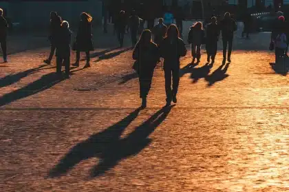 Silhueta anónima a seguir uma menina à distância numa rua urbana ao crepúsculo