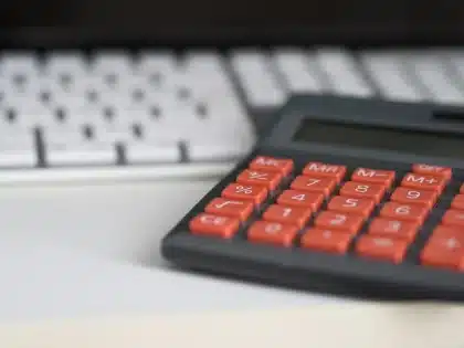Mãos a calcular impostos com documentos e calculadora numa secretária