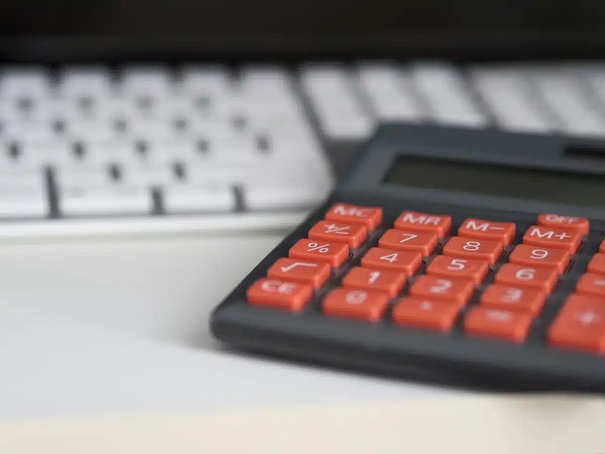 Mãos a calcular impostos com documentos e calculadora numa secretária
