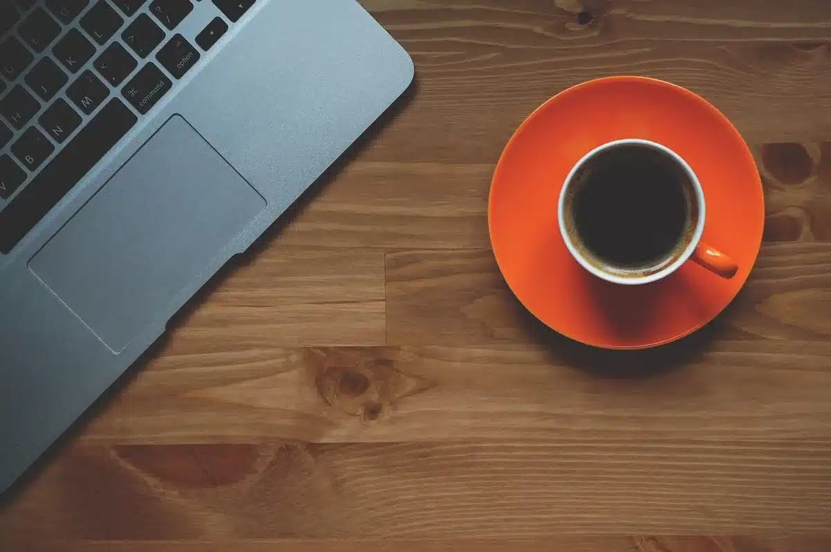 Mesa de trabalho com portátil exibindo gráficos, papéis com números e caneca de café