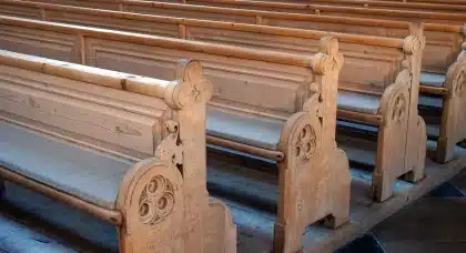 Interior de igreja com bancos de madeira, Bíblia gasta e vela votiva acesa
