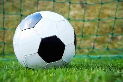 Silhuetas anónimas de adeptos junto a um estádio, bandeira desfocada ao fundo