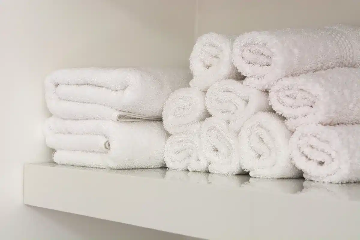 Mãos anónimas a segurar fios de cabelo sobre uma toalha numa casa de banho bem iluminada