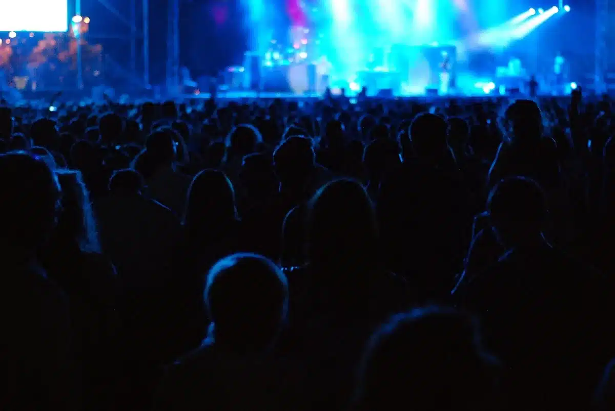 Público de concerto com murmúrios e reações, faces não identificáveis